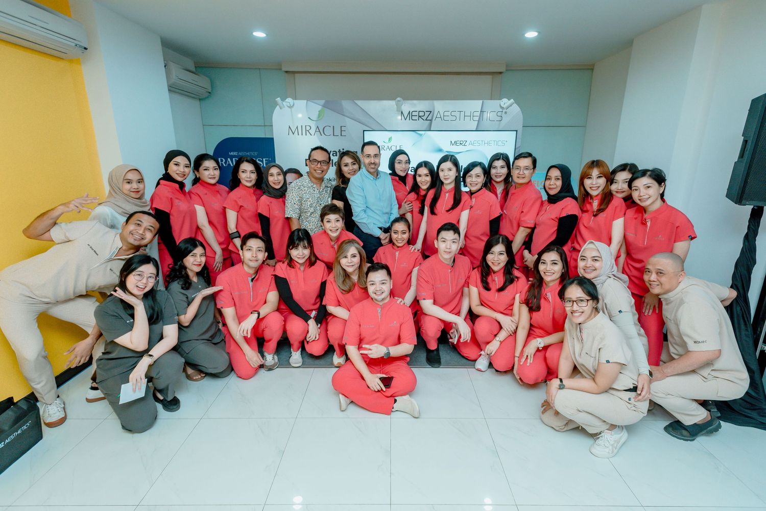 A group in matching red and beige uniforms pose together in a bright room for a team photo.