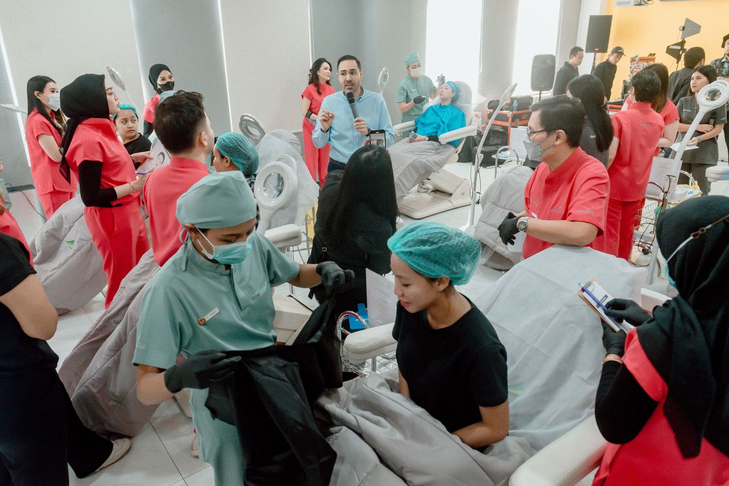 Healthcare workers in red and surgical scrubs gather in a crowded medical facility during a busy session.