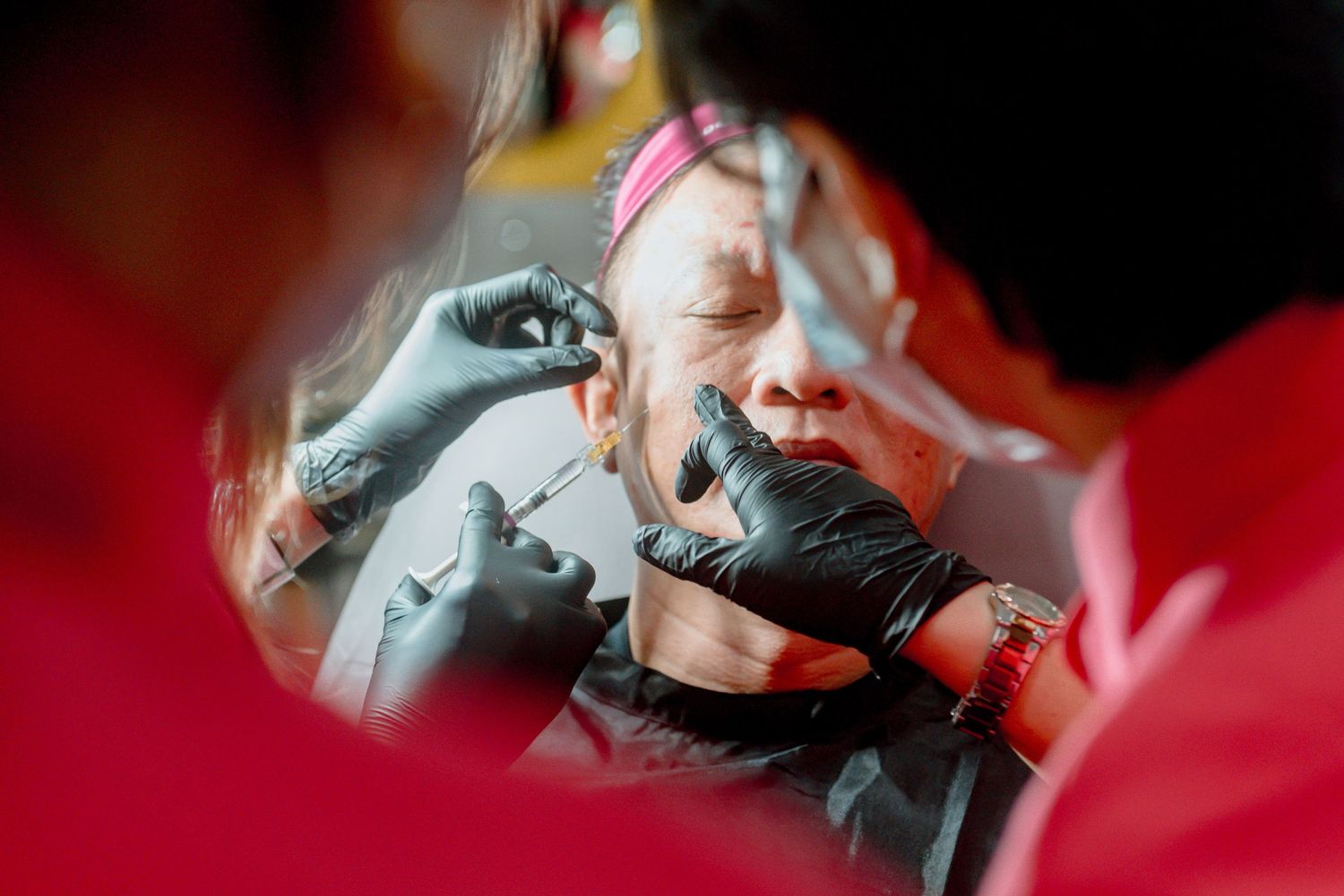 A reflection in a car mirror shows someone applying makeup with a pink headband against a dark background.