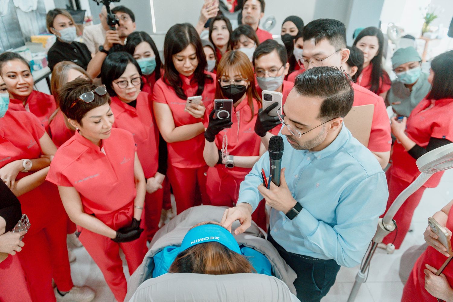 Healthcare professionals in red uniforms gather around a medical demonstration with an instructor in light blue.