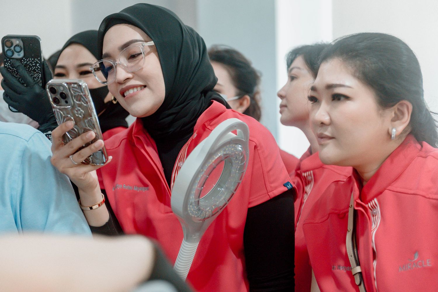 A group in red uniforms gather around to look at a mobile phone during an event.