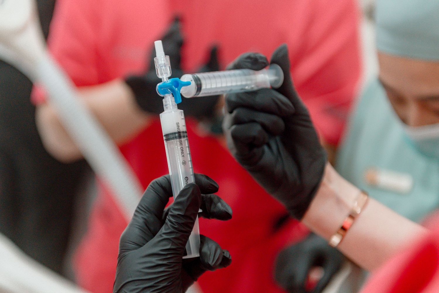 Healthcare worker wearing black gloves prepares a medical syringe with red background.