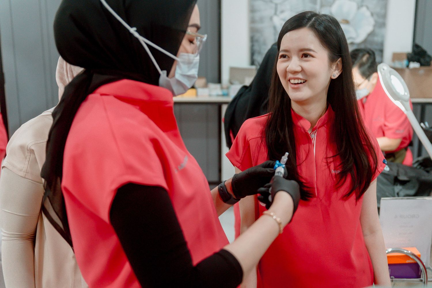 Two people in bright red jackets interact cheerfully in what appears to be a retail or service environment.