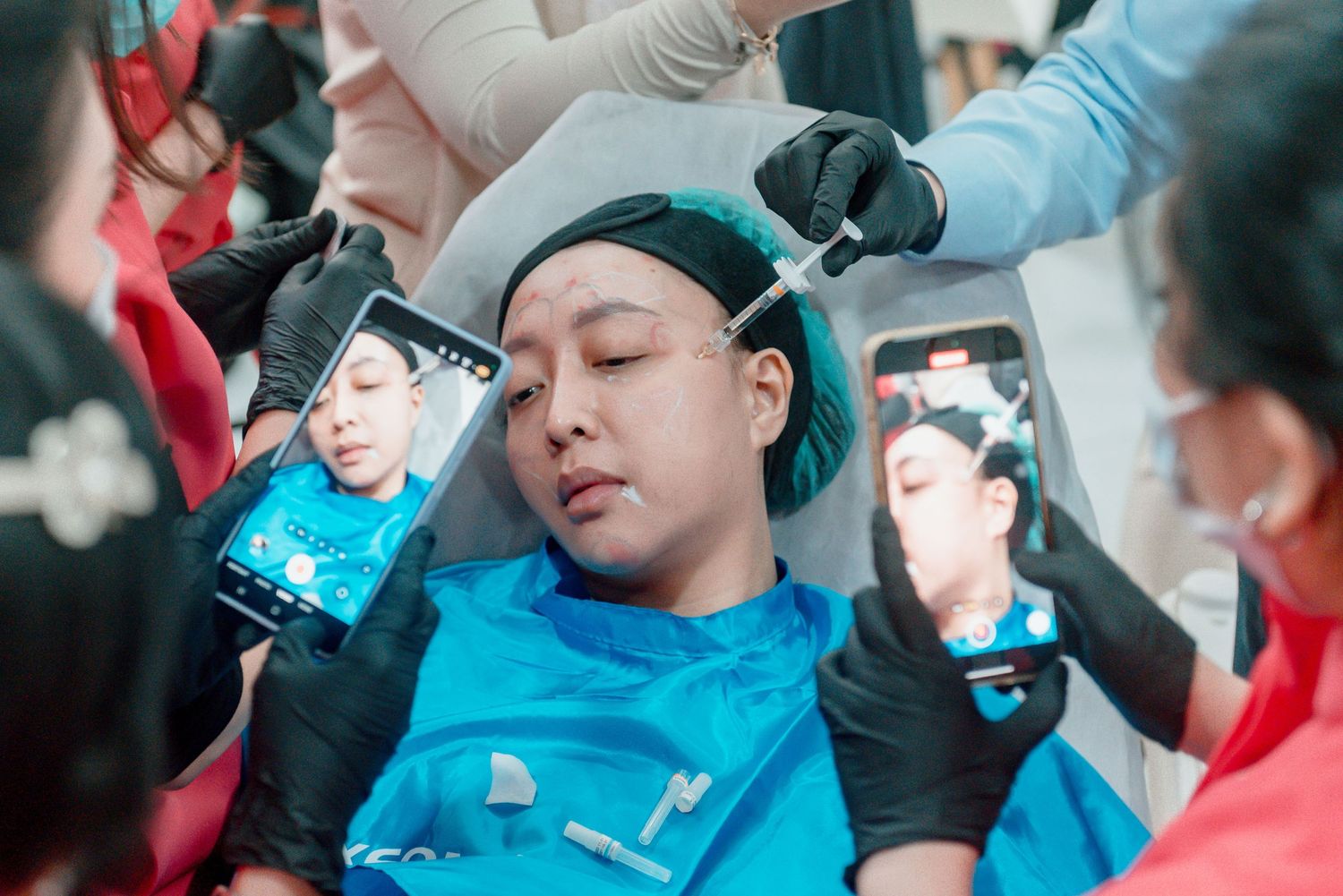 Multiple phones held up to record someone wearing a blue shirt and beanie lying down during a medical procedure.