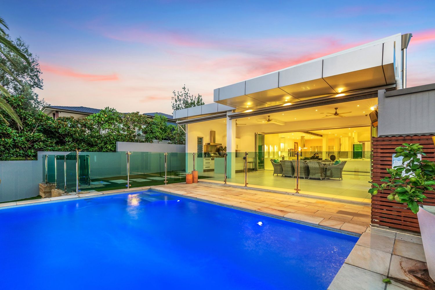 Luxurious outdoor pool with open-plan living area and glass walls at twilight.