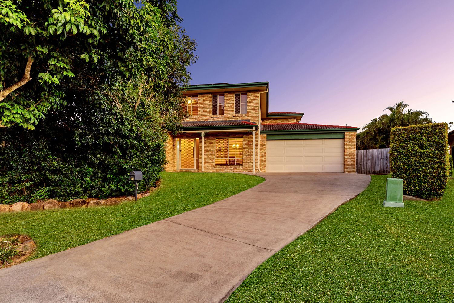 Two-story brick home with attached garage, curved driveway, and manicured lawn at dusk.