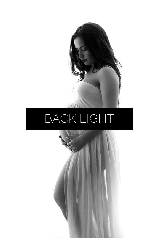Artistic black and white maternity silhouette series showing pregnant woman in flowing white dress against dark background.