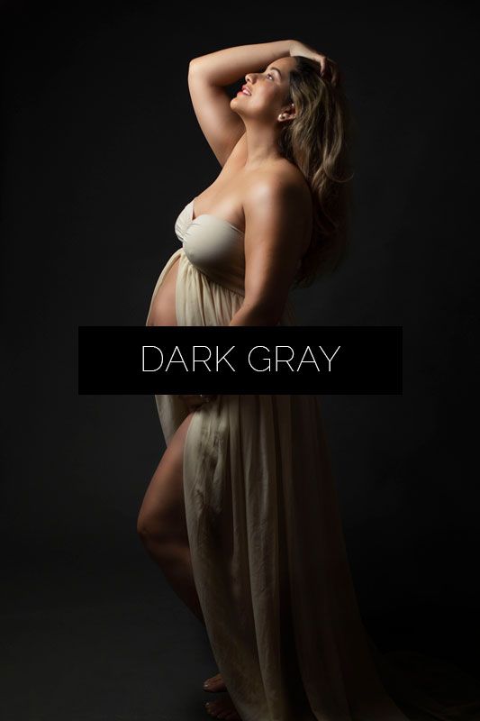 Artistic maternity photography series showing silhouette in dark gray flowing dress against black background.