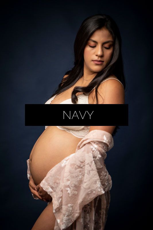 Elegant maternity portrait series featuring flowing lace fabric in navy blue studio setting.
