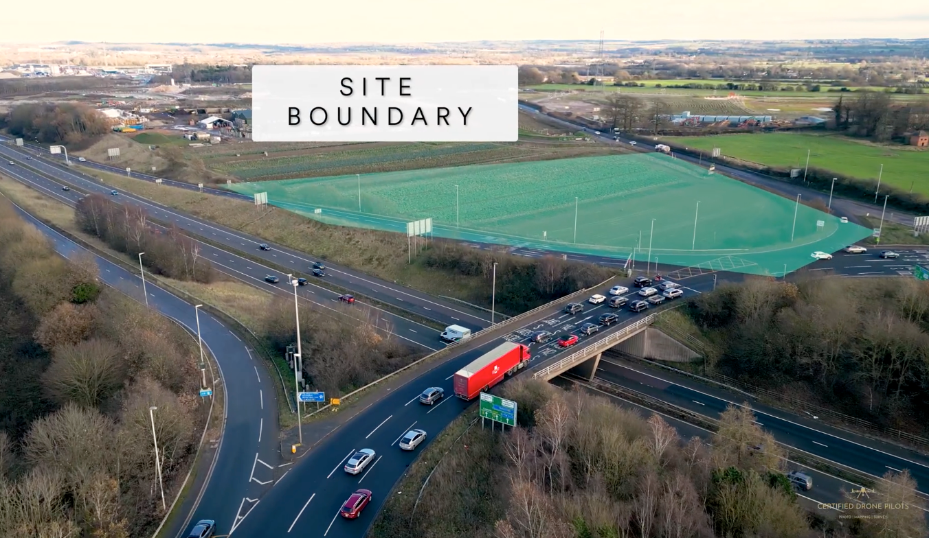 Aerial view of a site boundary near a busy road junction with sports fields and green spaces visible in the background.