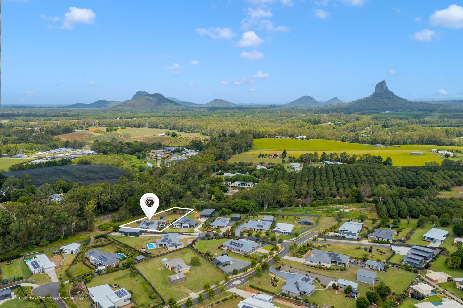 Aerial view of Queensland property with stunning Glass House Mountains panorama, farmland, and residential neighborhood.