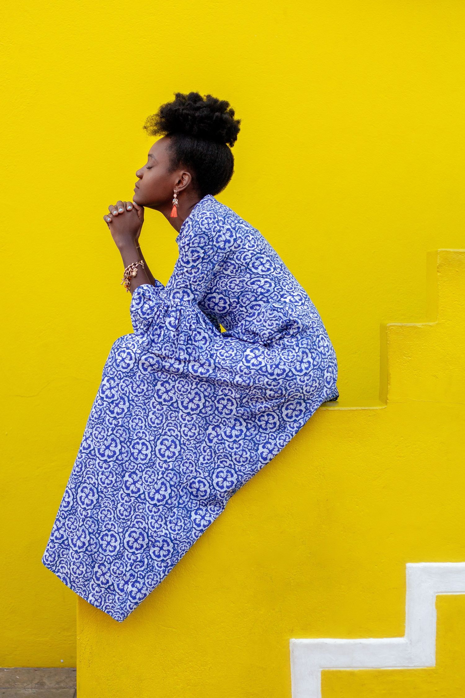 Fashion poses against a bright yellow wall wearing a blue and white patterned top.