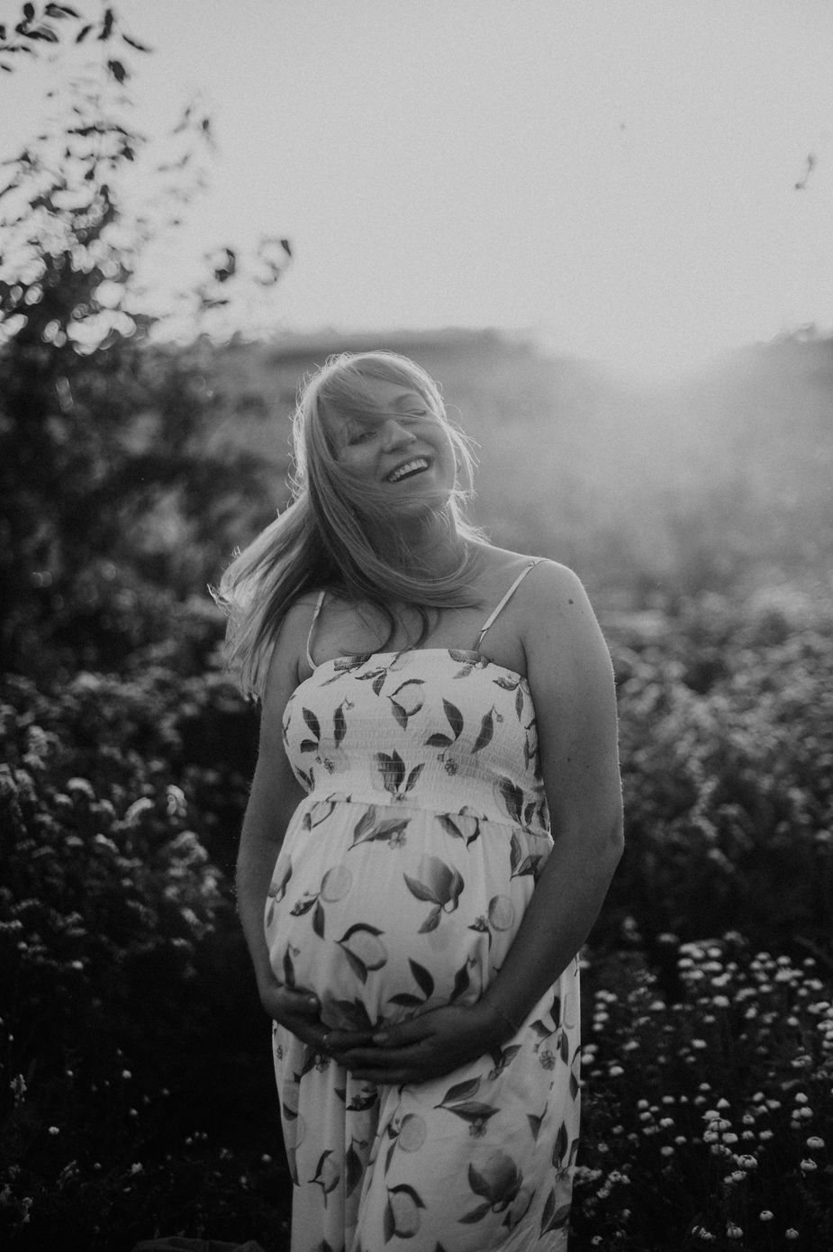 A person in a floral dress stands thoughtfully in a sunlit meadow of wildflowers during golden hour.