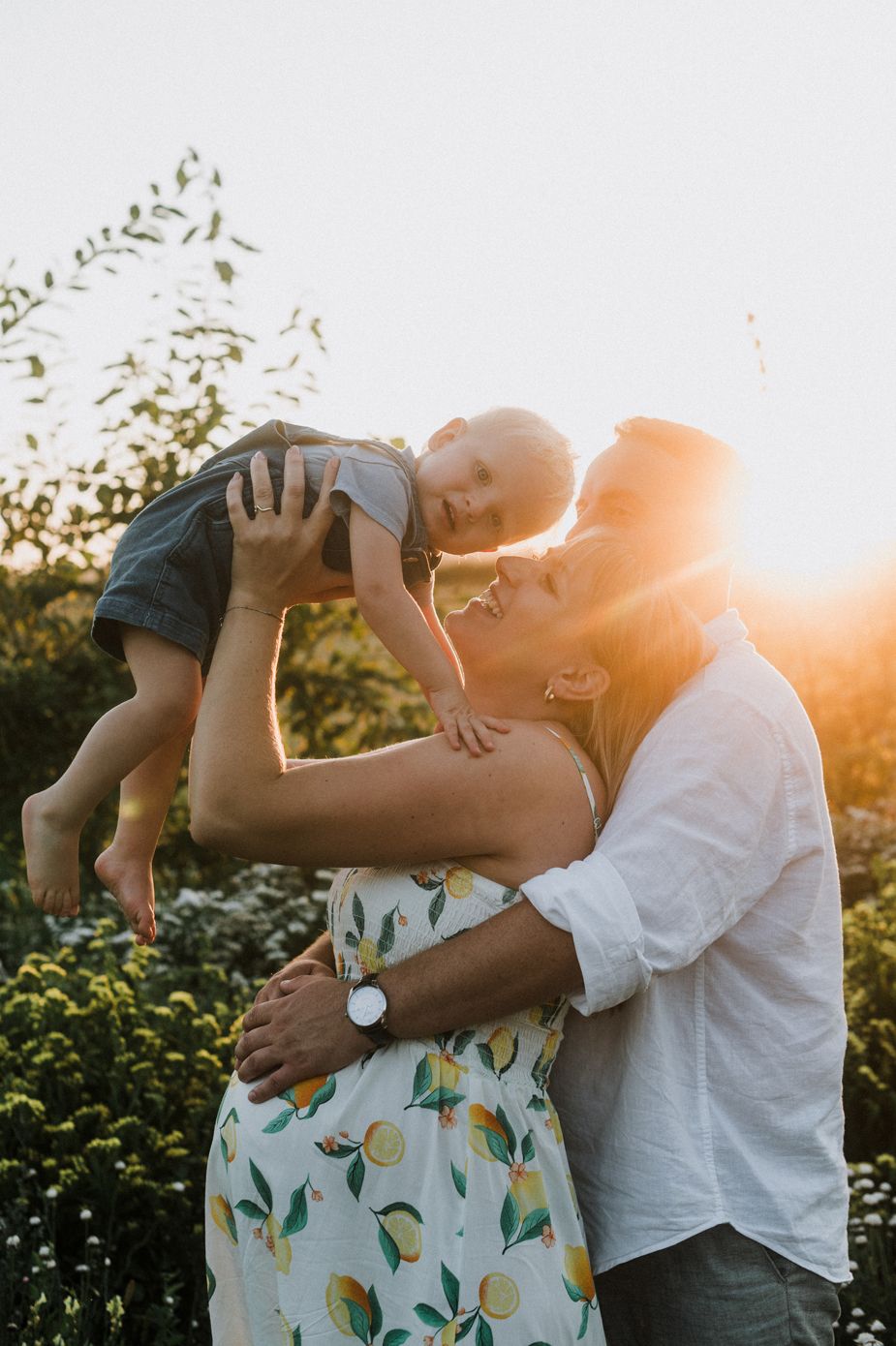 A loving family moment captured at sunset in a garden with golden sunlight streaming through trees and foliage.