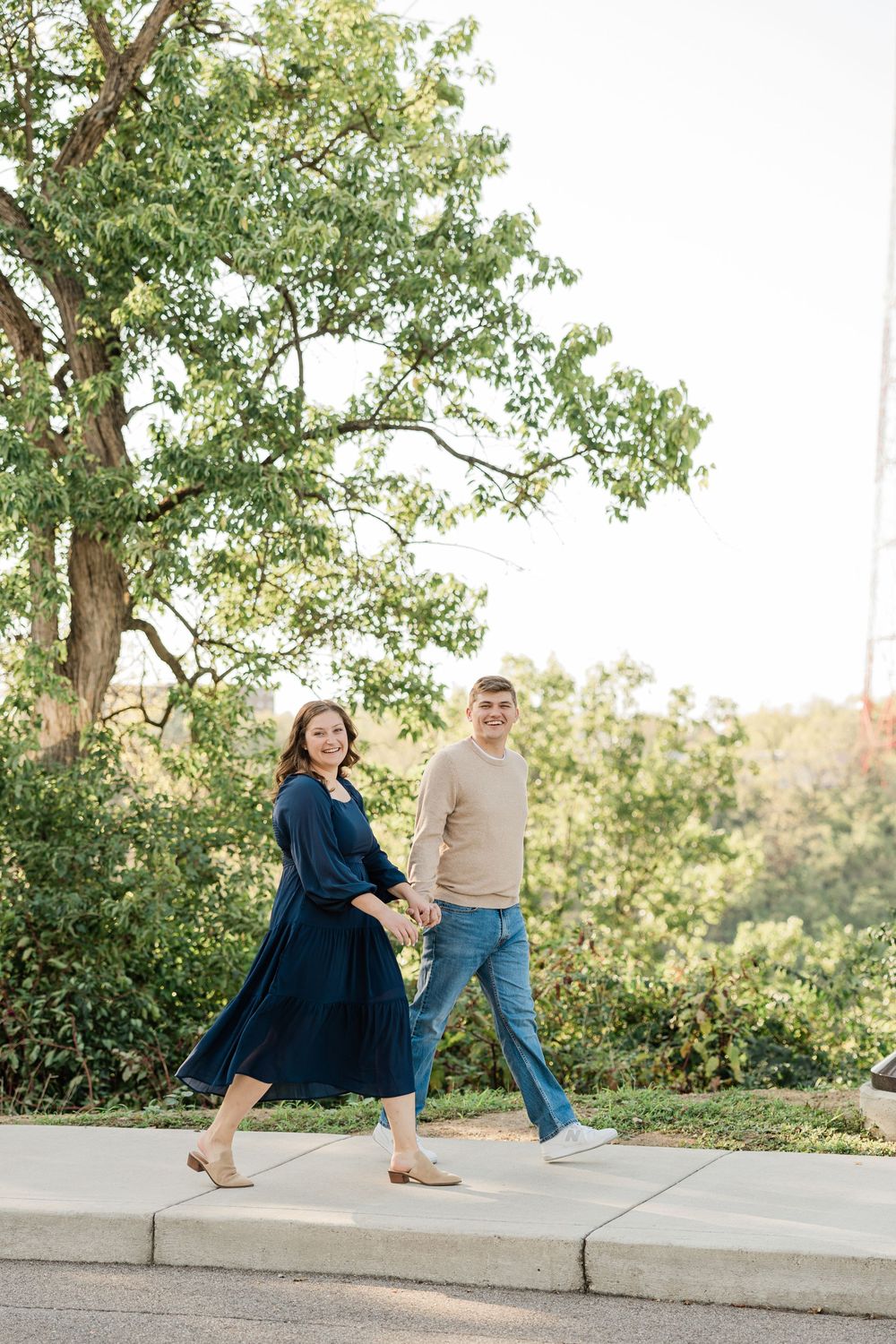 A couple walks hand in hand on a path wearing navy and beige outfits.