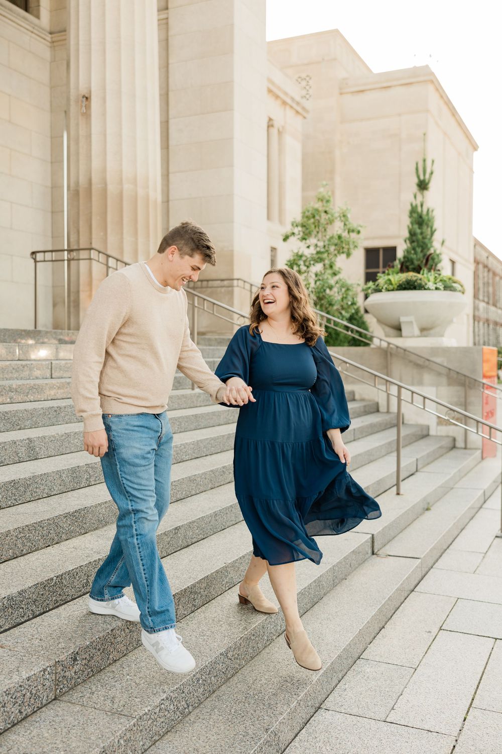 A couple laughing together while walking down stone steps outside a building.