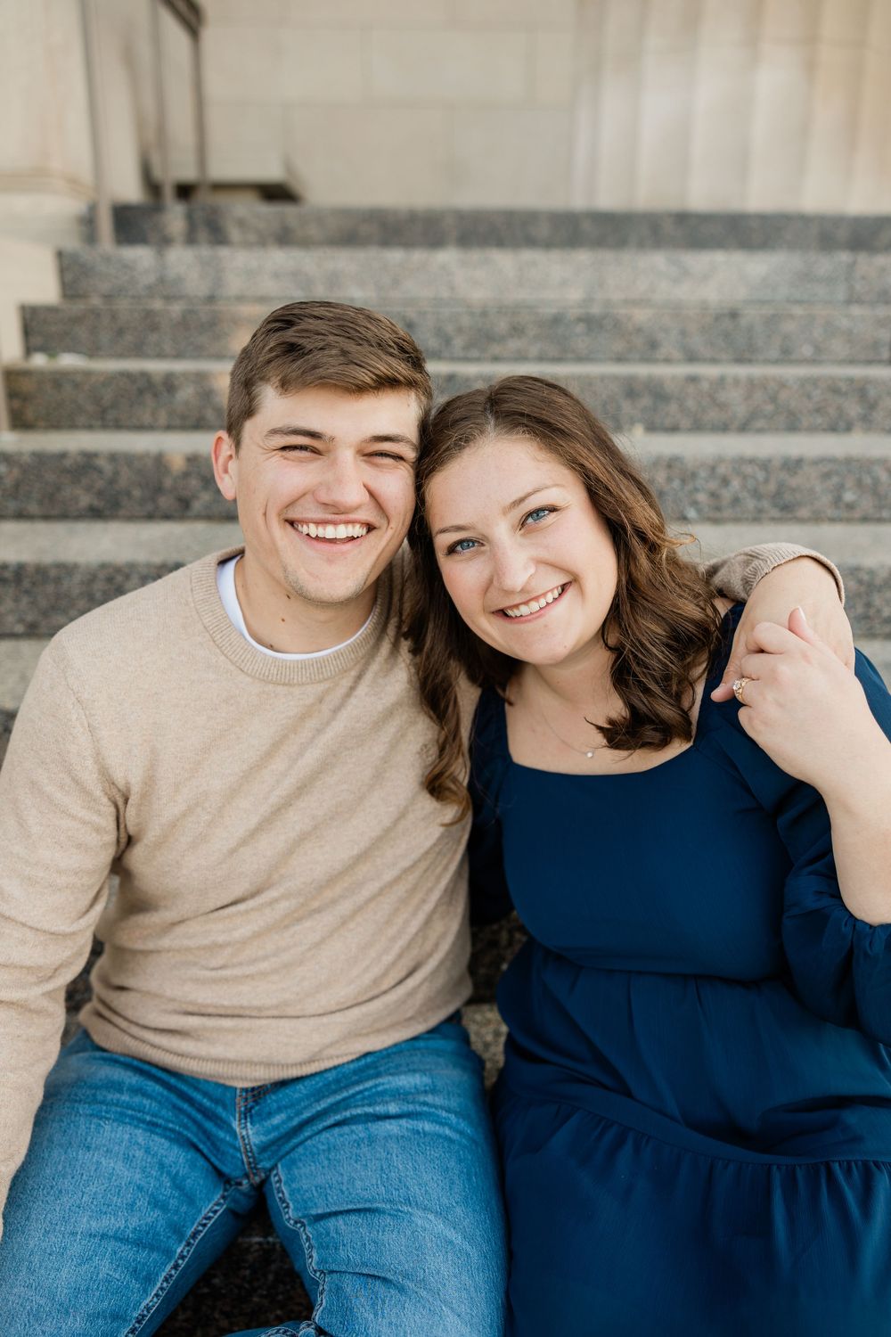 A couple sits together on concrete steps, wearing coordinating blue and beige outfits.