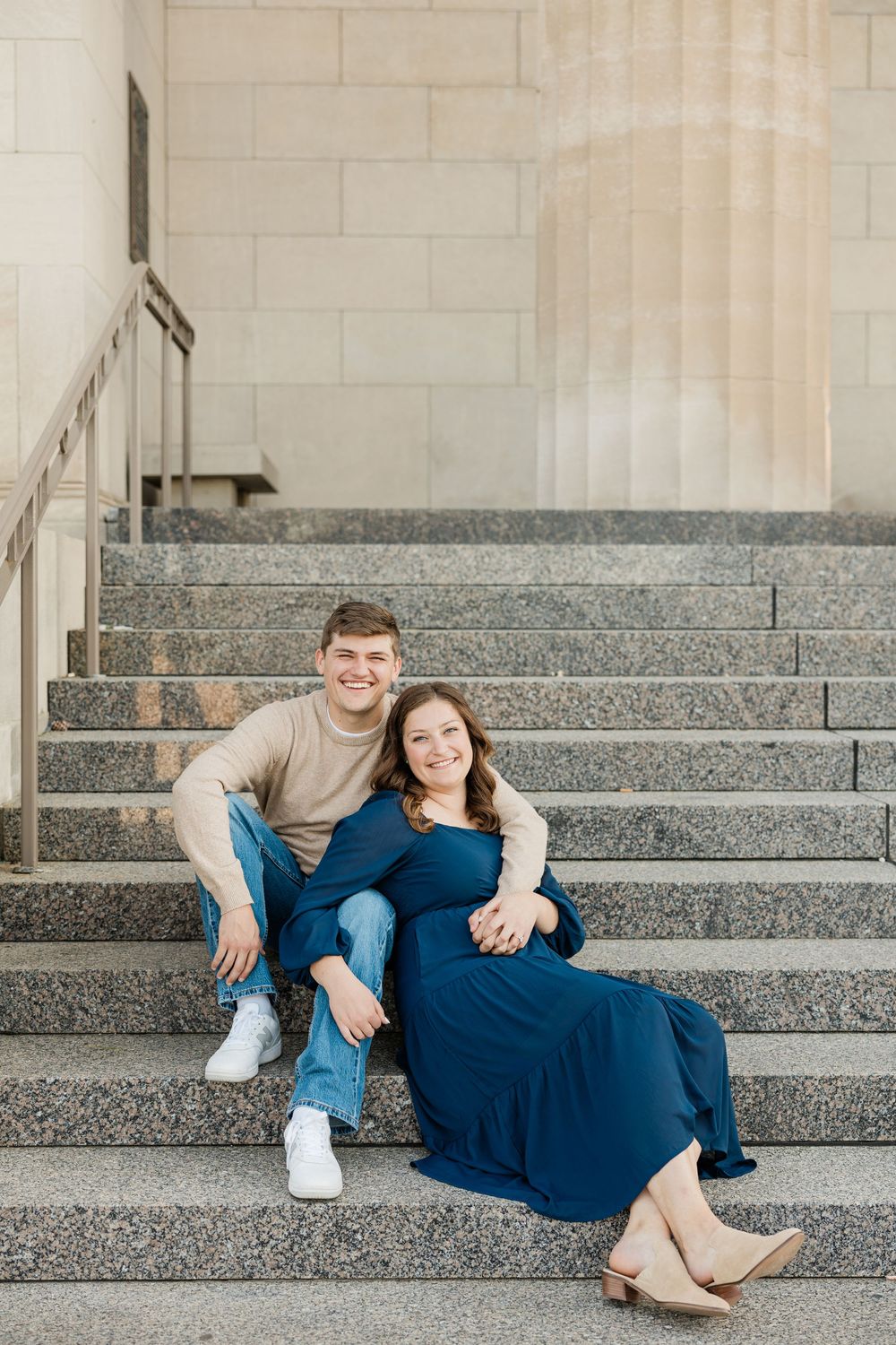 A couple relaxes together on concrete steps in coordinating blue outfits.