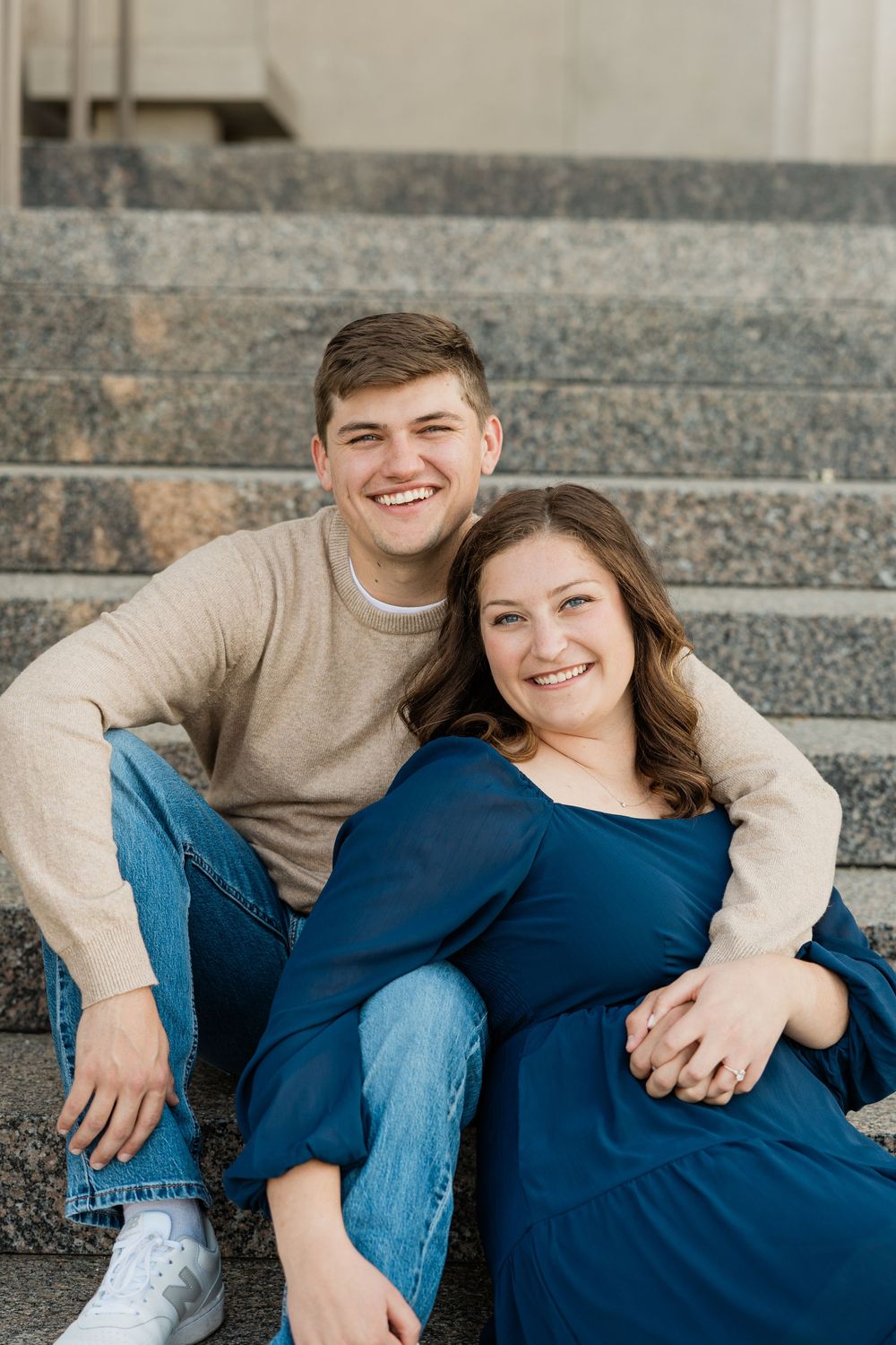 Casual couple relaxing on concrete steps outdoors wearing blue and beige clothing.