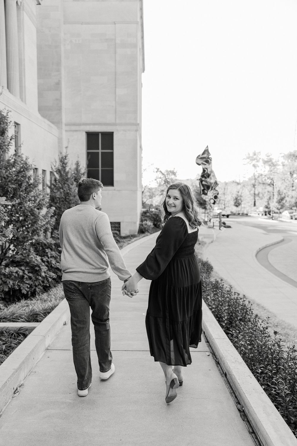 Black and white photo of a couple walking together on a paved path beside a building.