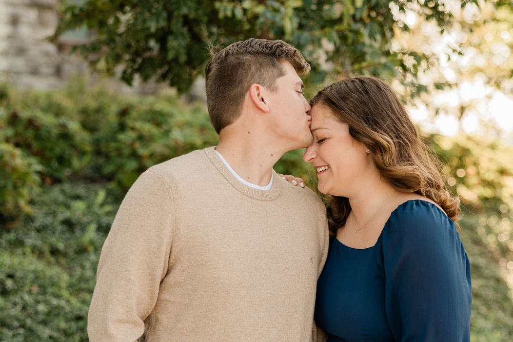 A tender moment between a couple wearing casual sweaters against greenery.