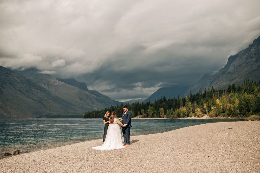 A wedding celebration takes place on a scenic beach with dramatic mountains and moody clouds at Lake Wakatipu, New Zealand.
