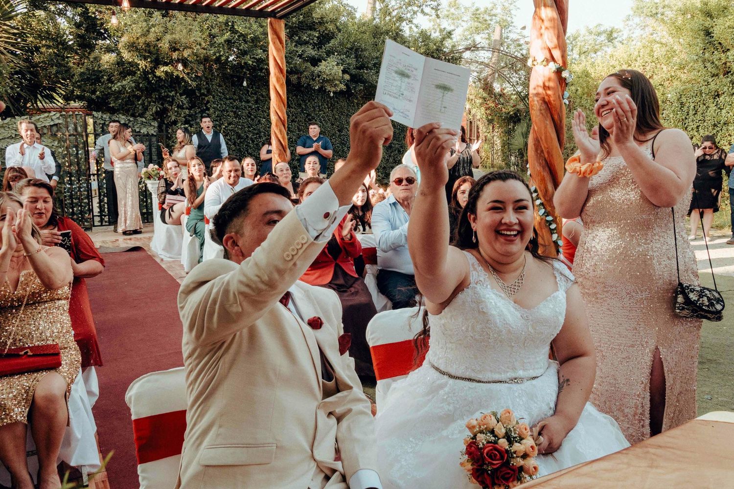 Fiesta de matrimonio al aire libre bajo luces colgantes y pérgola de madera con invitados celebrando.