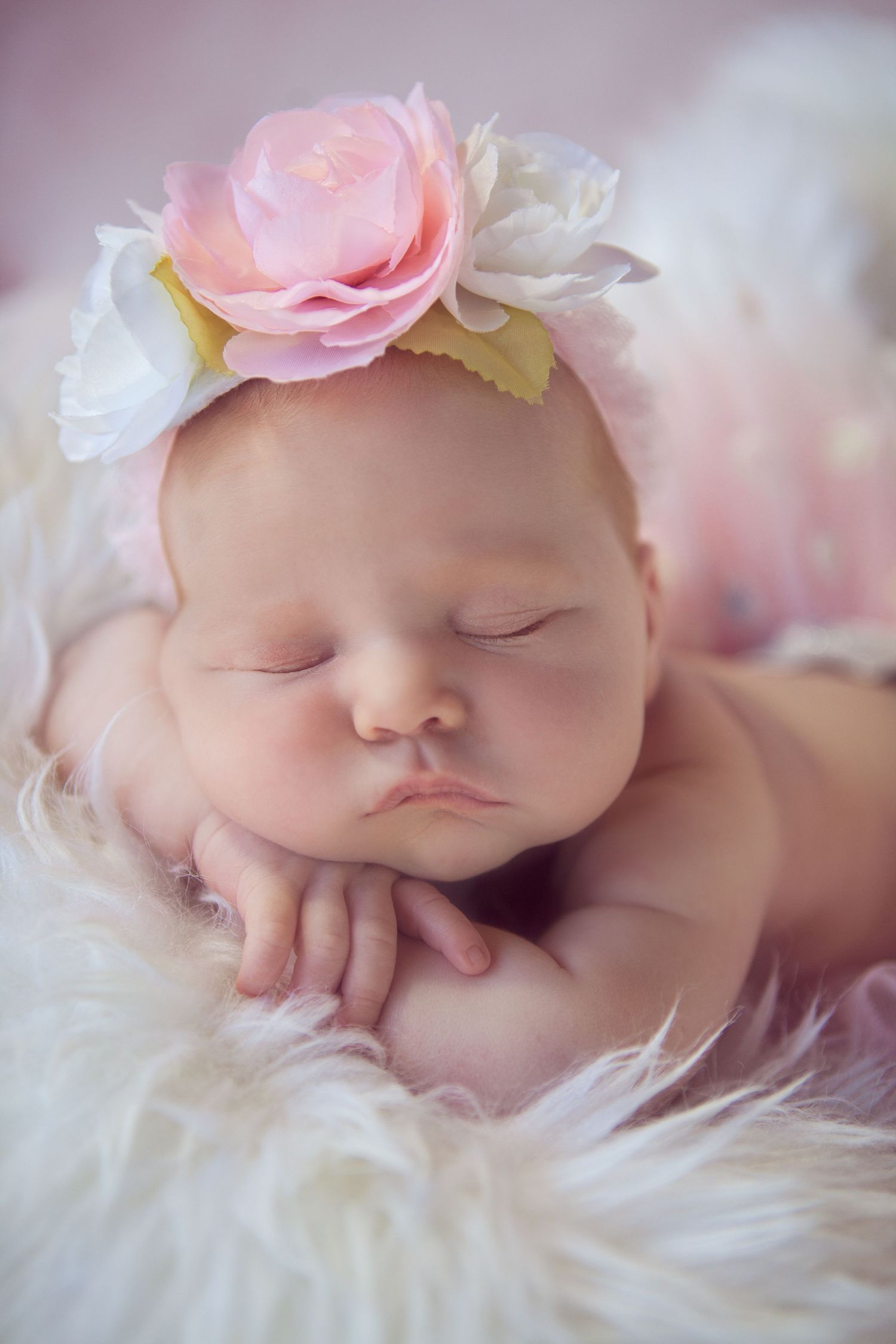 Sleeping baby wearing a pink floral headband on soft white fur.