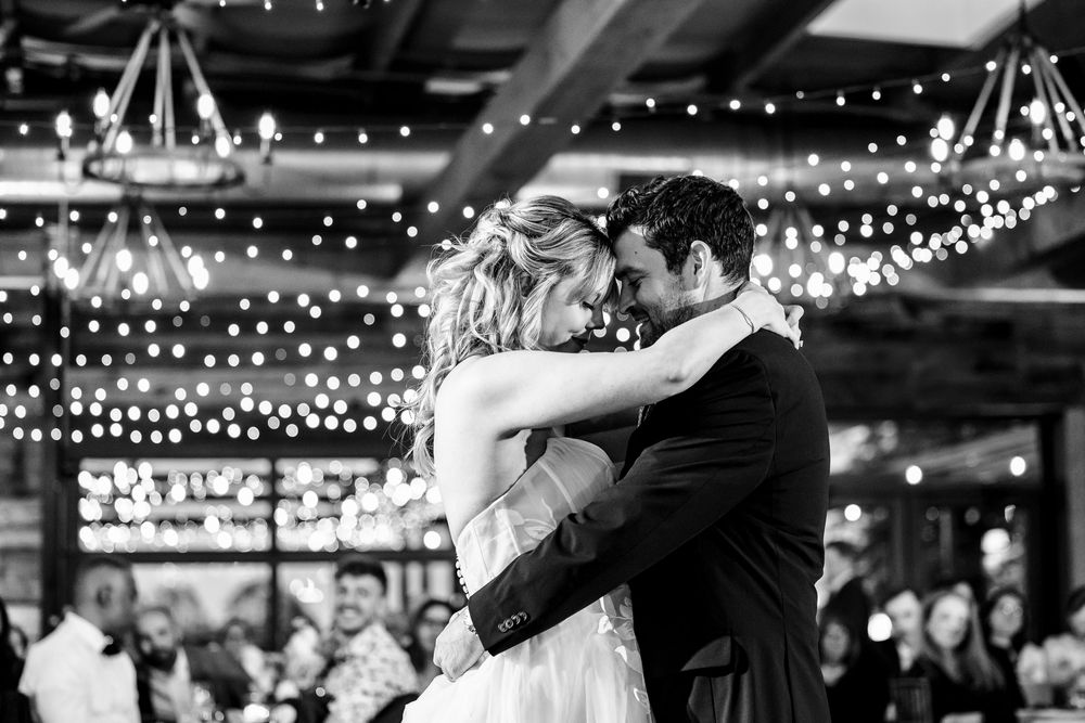 A romantic black and white photo of a couple's first dance under twinkling reception lights.