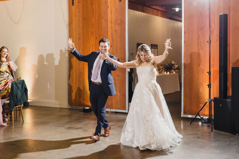 Wedding guests dancing and celebrating in a spacious venue with wooden walls.