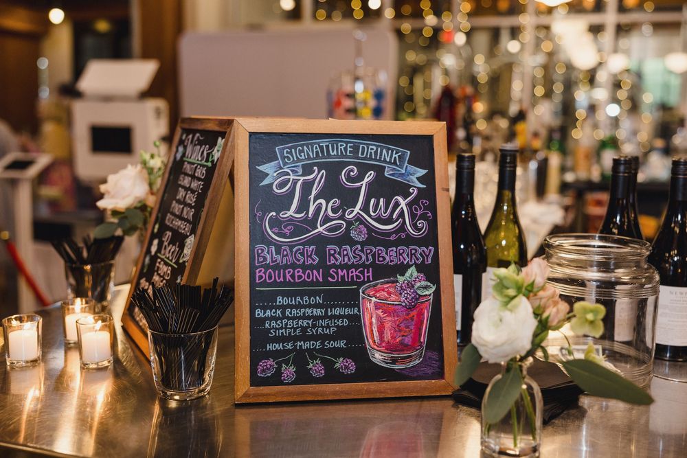 Wedding reception bar setup with chalkboard drink menus and candlelit ambiance.
