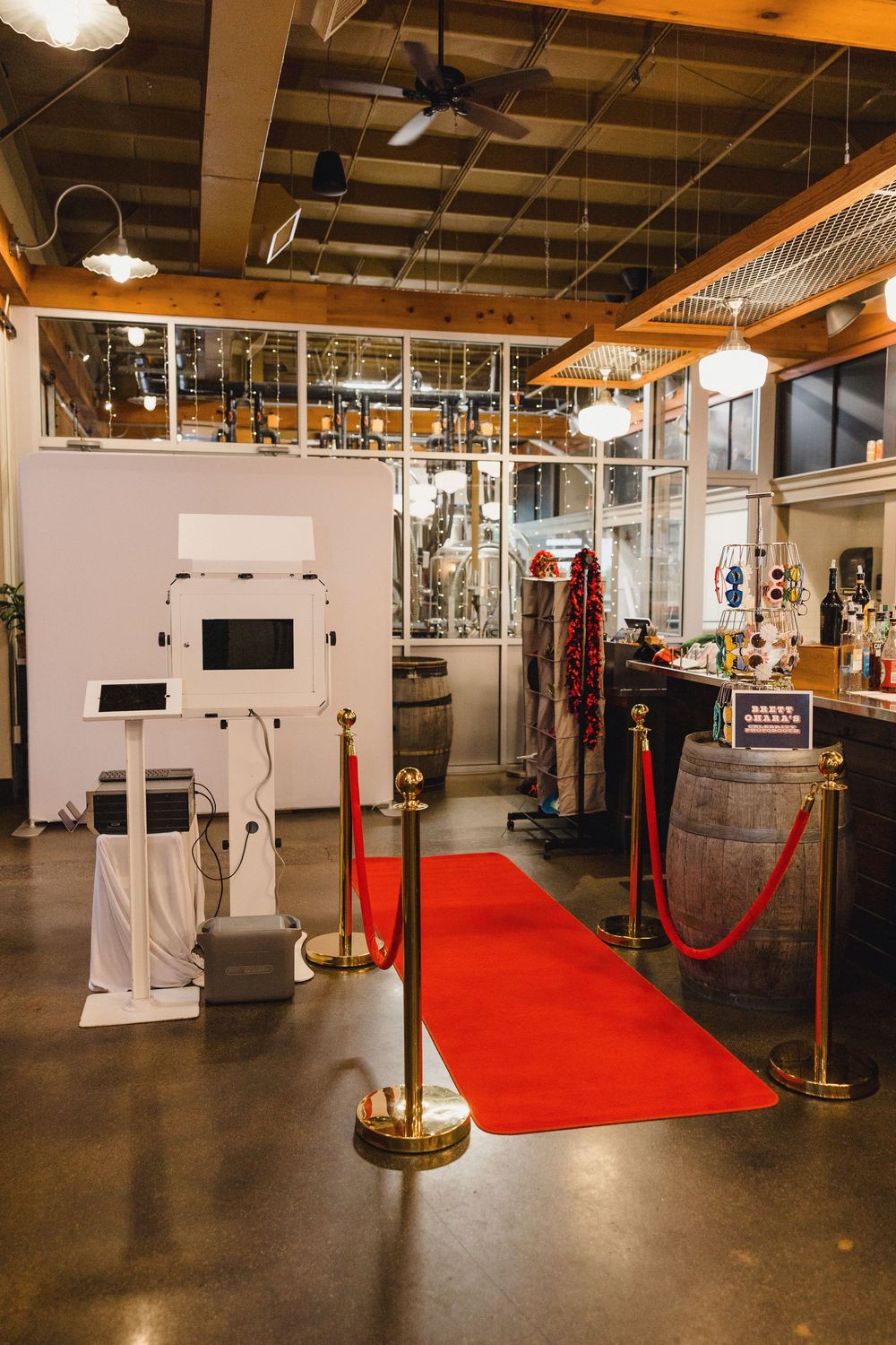 A modern photo booth setup with a red carpet and stanchions in an industrial-style space with exposed ceiling beams.