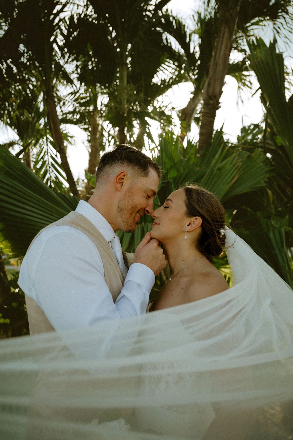 Romantic wedding couple shares intimate moments against a backdrop of tropical palm trees at sunset.