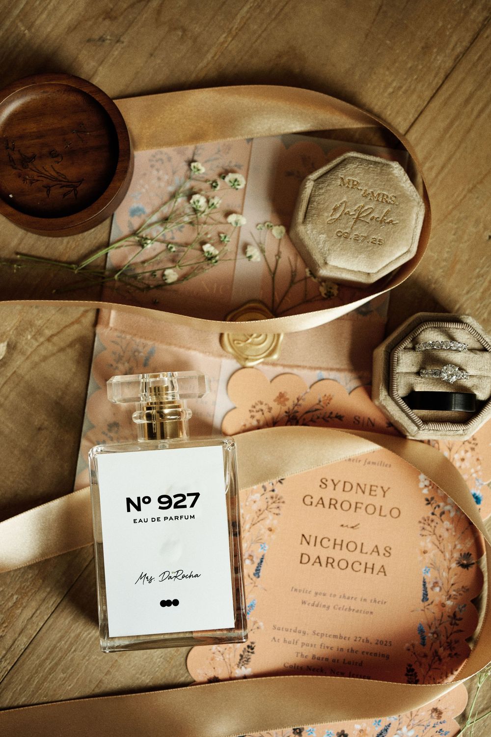 Elegant wedding flat lay featuring perfume, floral invitations, and ring boxes for Sydney and Nicholas.