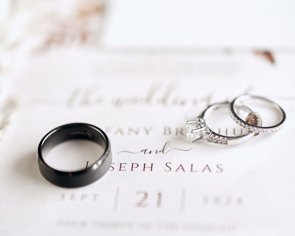 Wedding rings and diamond engagement ring displayed on elegant wedding invitation.