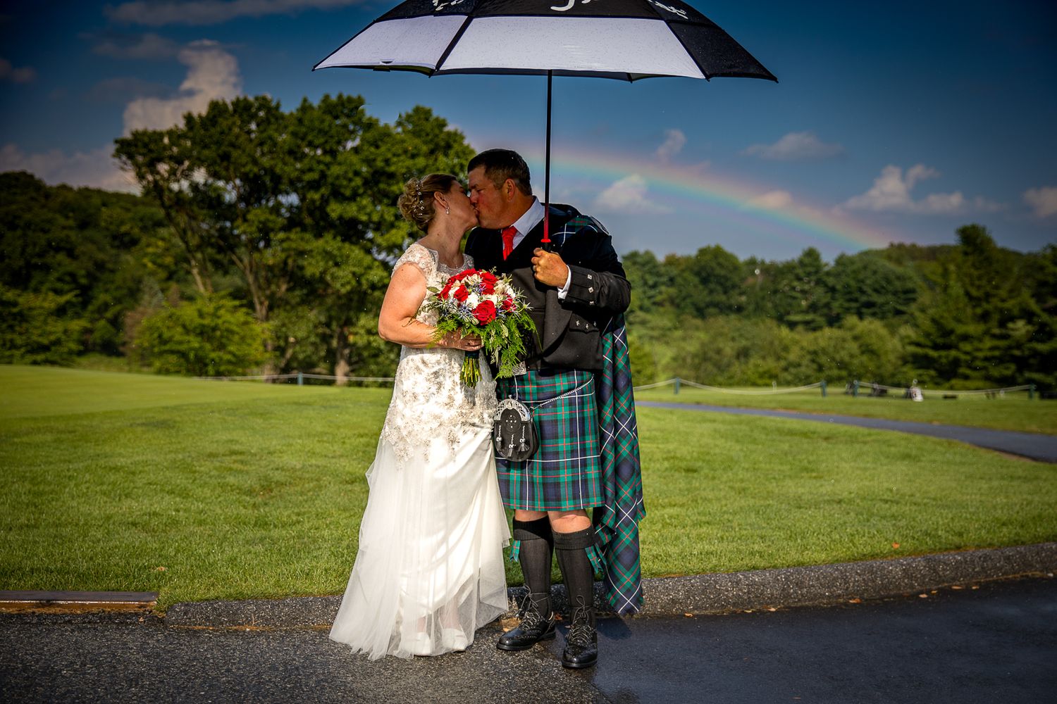 Frederick Maryland Wedding Photographer  Wedding couple shares romantic moment under umbrella on rainy day with Scottish kilt attire.