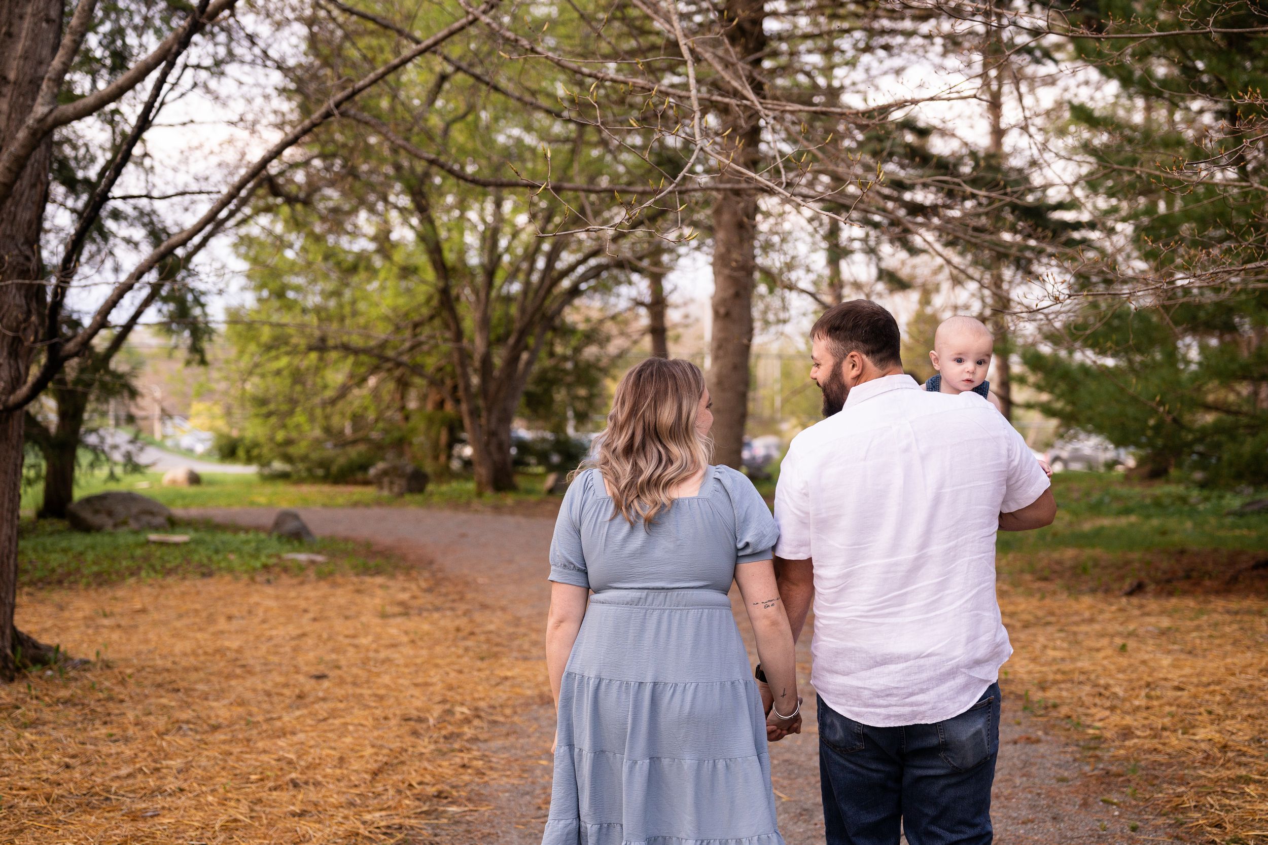 A couple walks hand in hand through a scenic autumn park with fallen leaves and tall trees along the path.