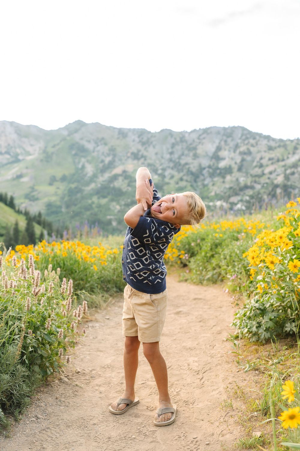 Child playing and laughing in a mountain meadow surrounded by bright yellow wildflowers on a sunny summer day.