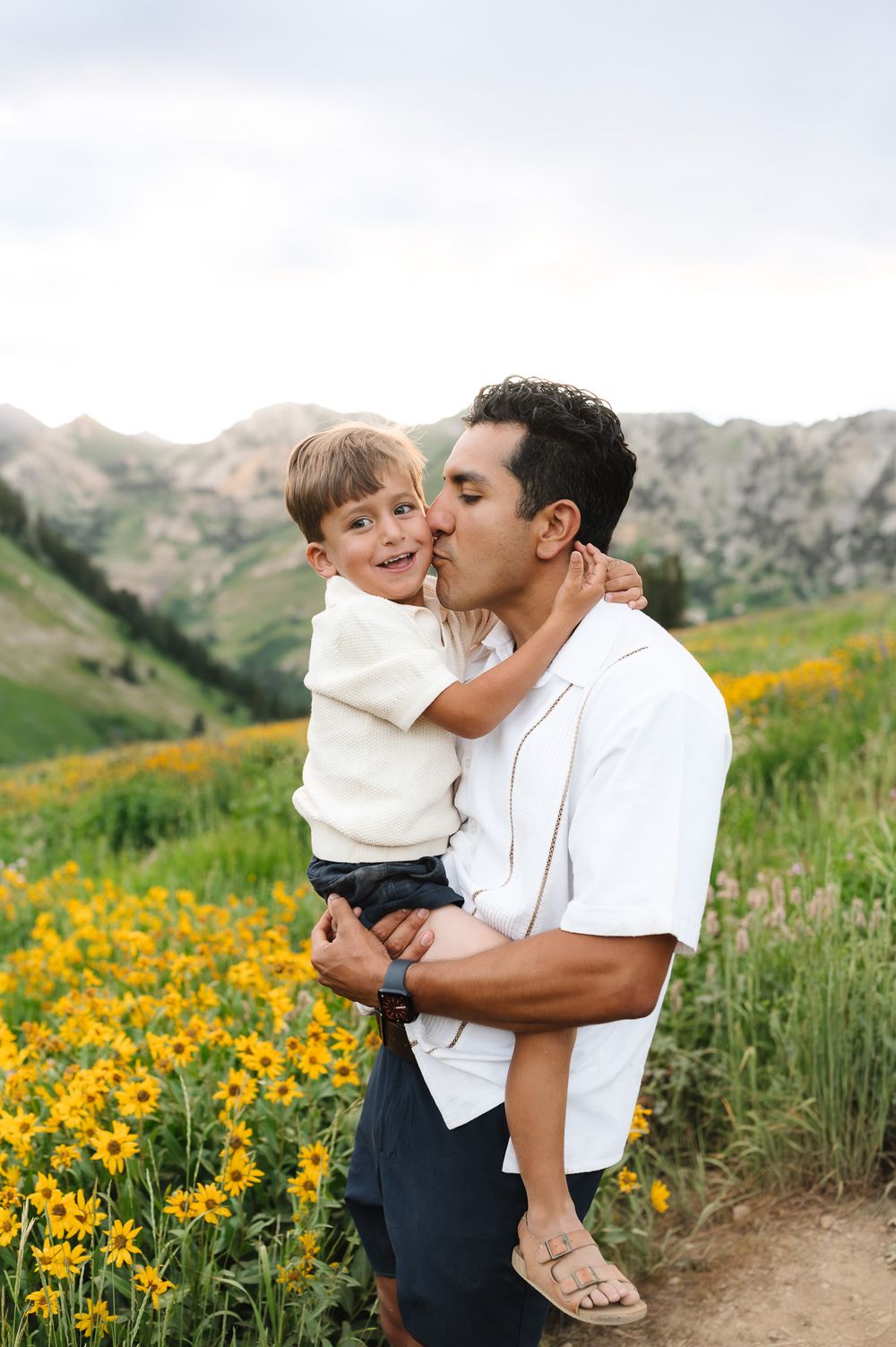 A parent and child share tender moments together against a backdrop of yellow wildflowers in the mountains.