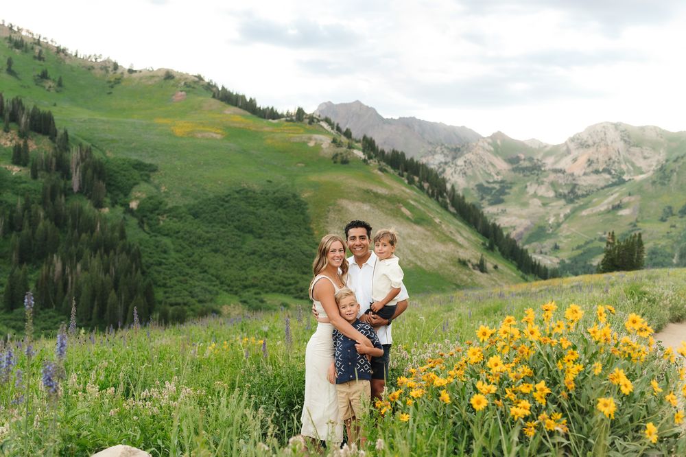 A couple poses together among vibrant yellow wildflowers with majestic mountain peaks in the background at Albion Basin.