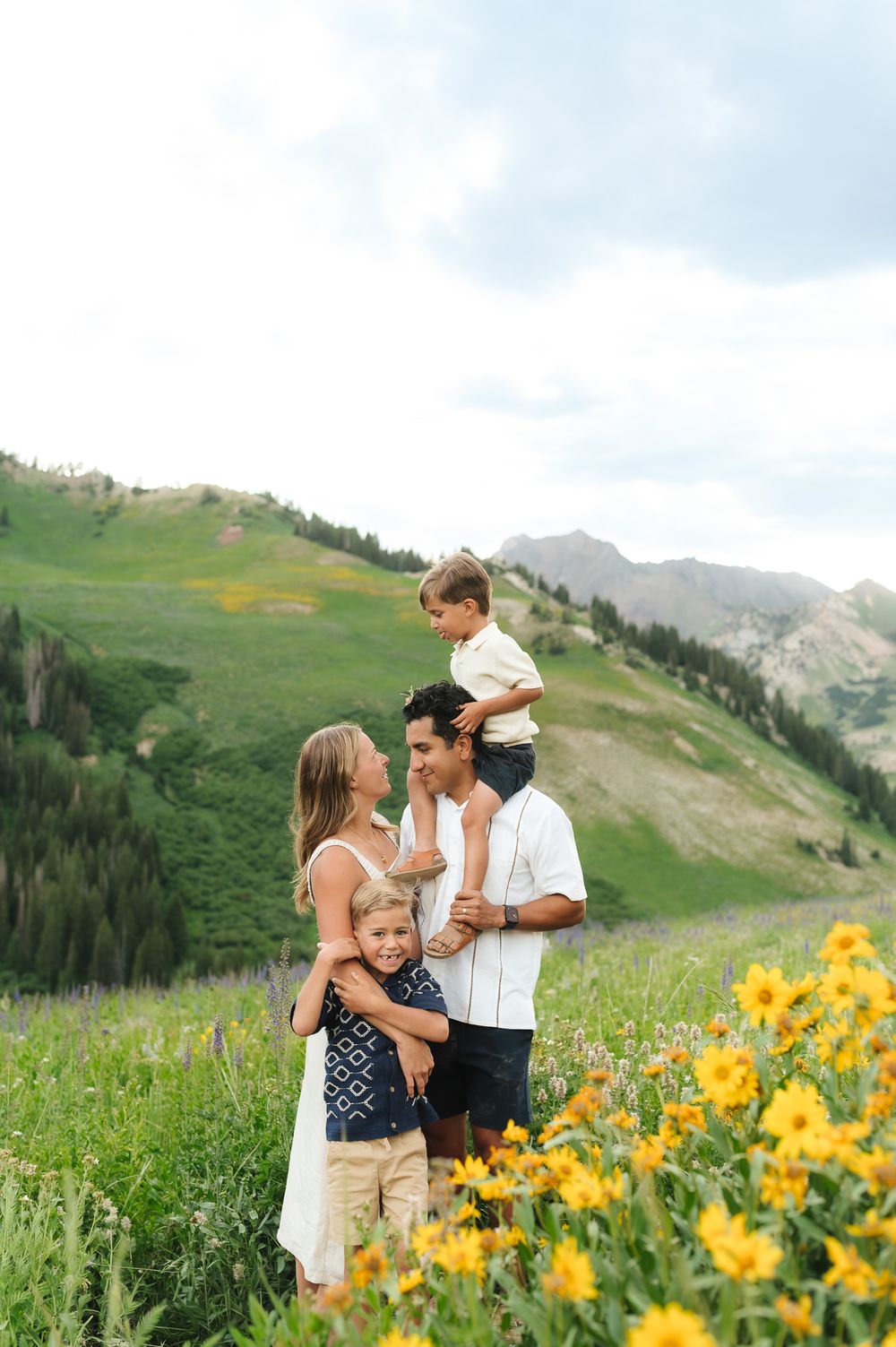 A family shares joyful moments together in a mountain meadow filled with vibrant yellow wildflowers.