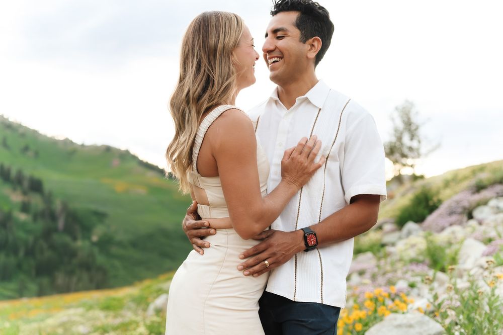 A couple shares a romantic moment while embracing outdoors in a scenic mountain meadow setting in Little Cottonwood Canyon.