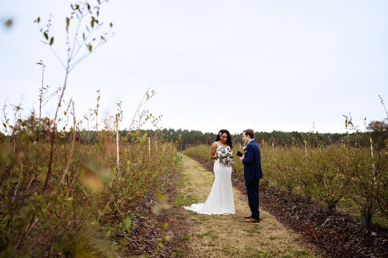Wedding couple poses for photos in a rustic outdoor setting with tall grasses and autumn foliage.