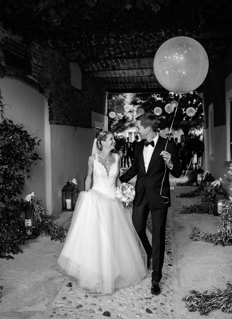 Bride and groom walking together under an archway holding a white balloon.