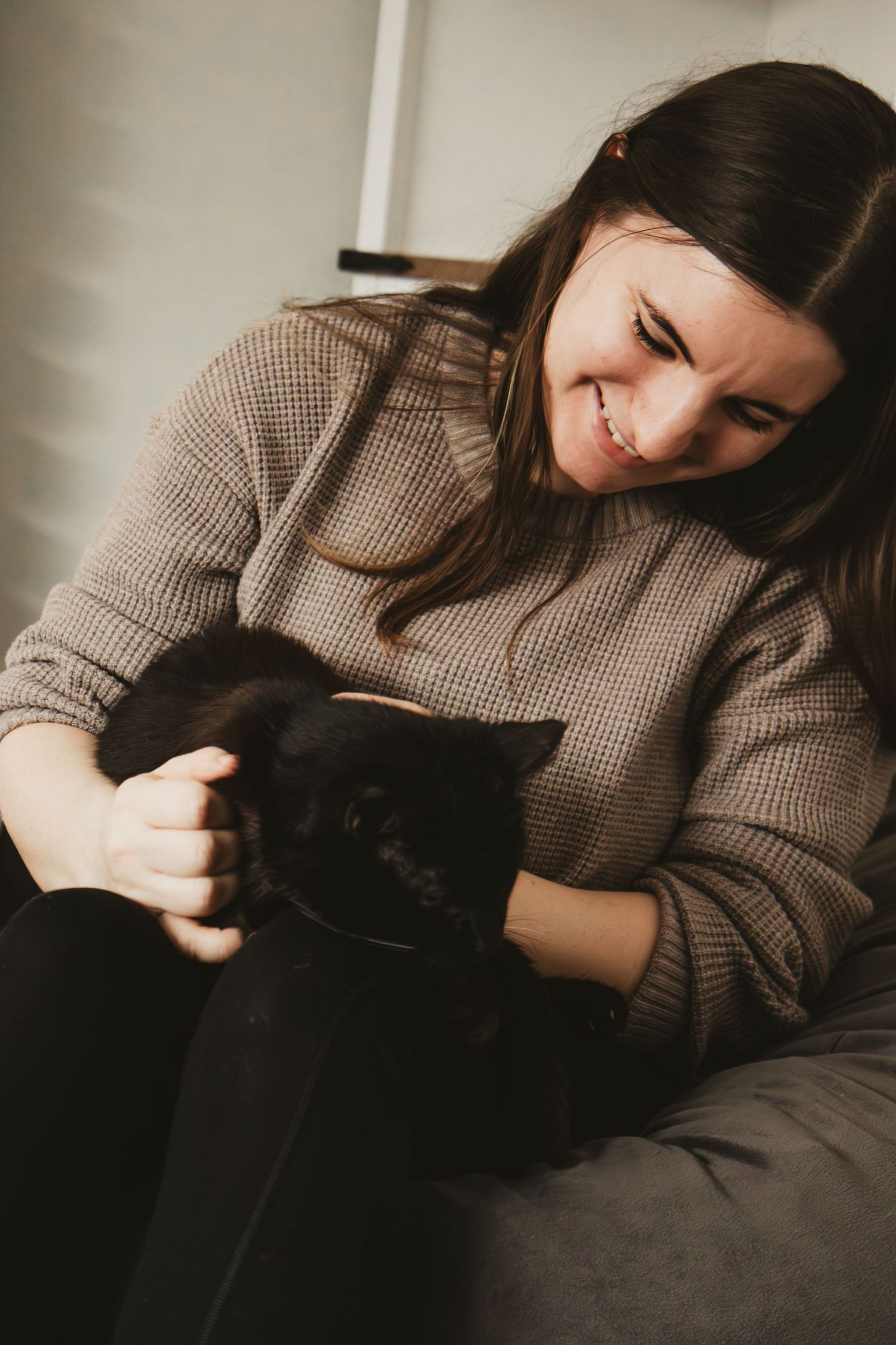 A person in a brown sweater lovingly cuddles with their black cat on a dark couch in a series of intimate moments.