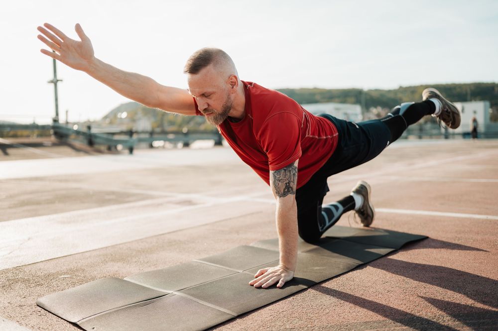 Person performing a plank exercise progression on an outdoor track surface during fitness training session.