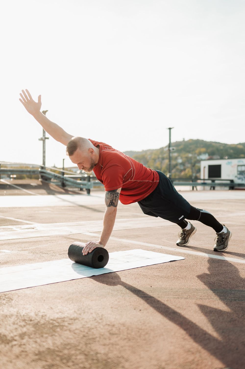Person in red shirt demonstrates burpee exercise progression on outdoor concrete surface in four sequential steps.