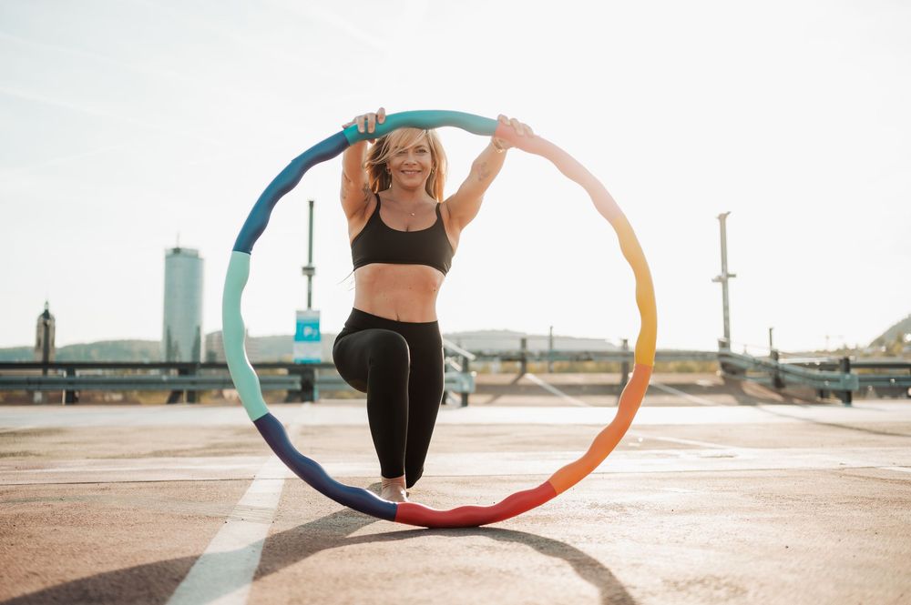 A person performs dynamic hoop movements with a colorful hula hoop in an outdoor setting during sunset.