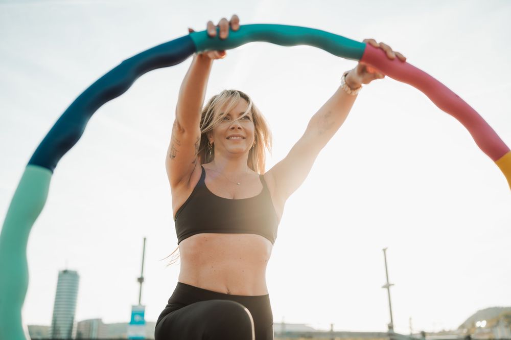 A person in workout attire holds up a colorful fitness band against a bright sky during an outdoor exercise session.