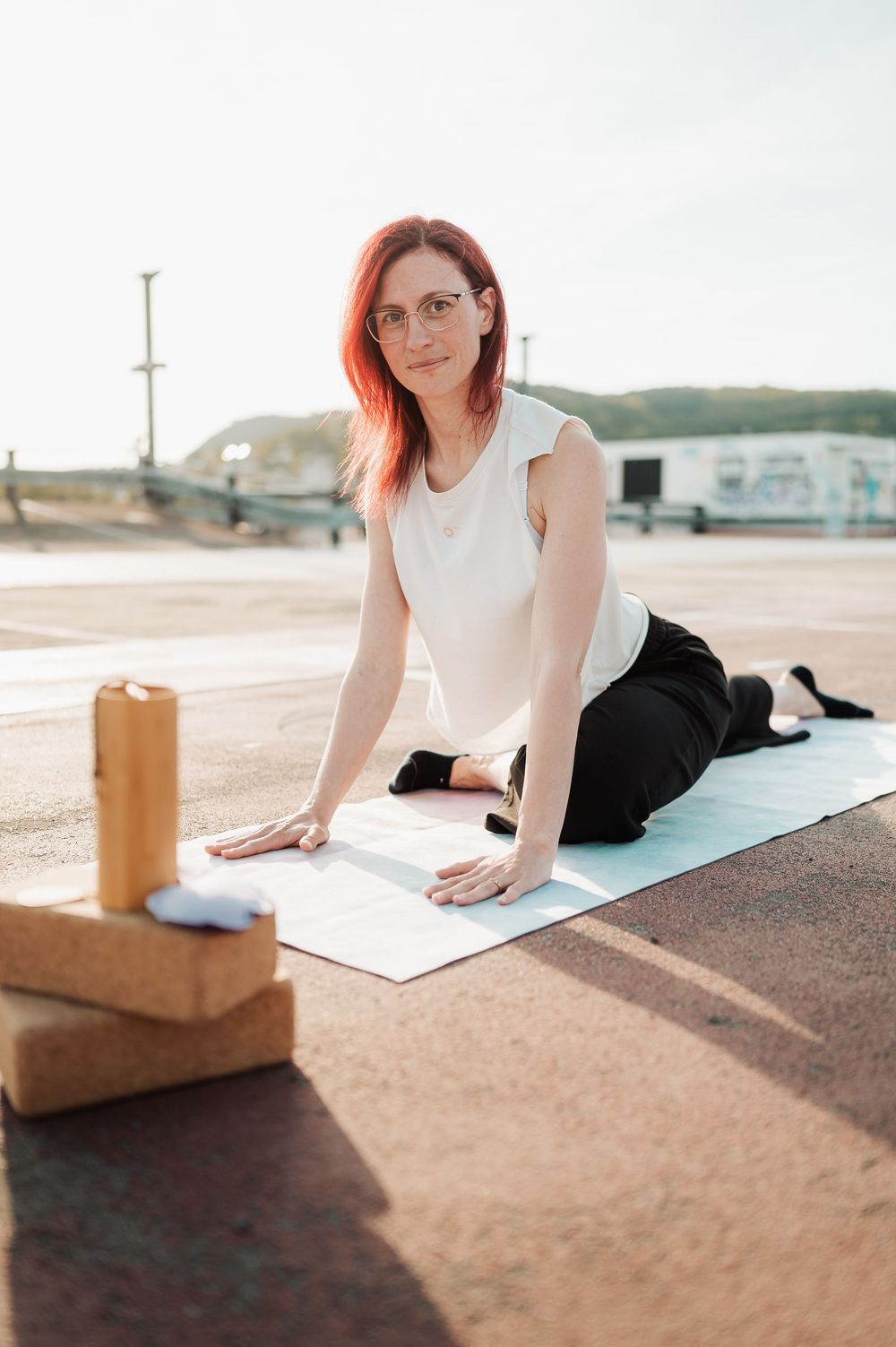 A person with red hair writing in a journal while sitting on a yoga mat at an outdoor beachside location.